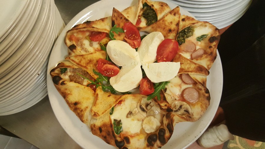 Pizza a stella di Lo Scugnizzo con punte ripiene di würstel e funghi, mozzarella, pomodorini e rucola al centro