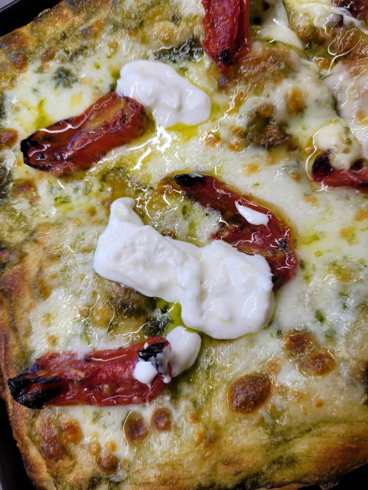 Pizza Lo Scugnizzo con pesto, mozzarella filante, burrata, pomodorini al forno e filo d'olio, bordi dorati in teglia scura